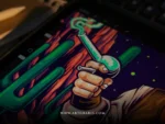 Close up of a hand holding a bong gun on the tablet with desert cliffs and cacti behind.